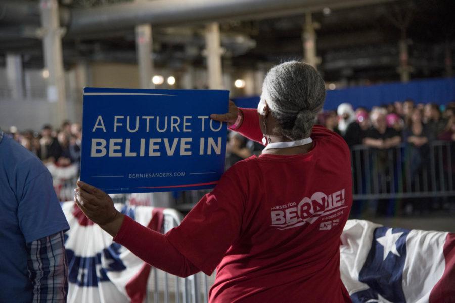A supporter holding a Sanders campaign sign wears a shirt that reads Nurses for Bernie!