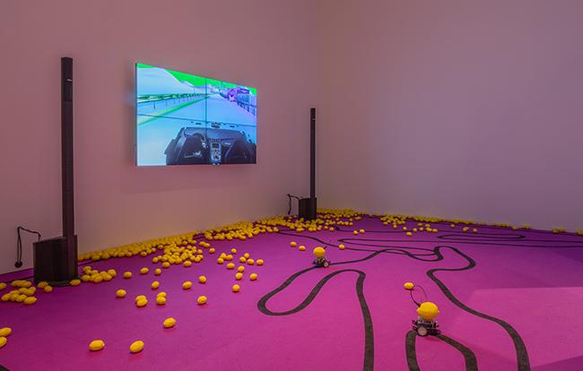 Plastic lemons are scattered across the floor in front of bizarre animations in Youngs installation, The highway is like a lions mouth.