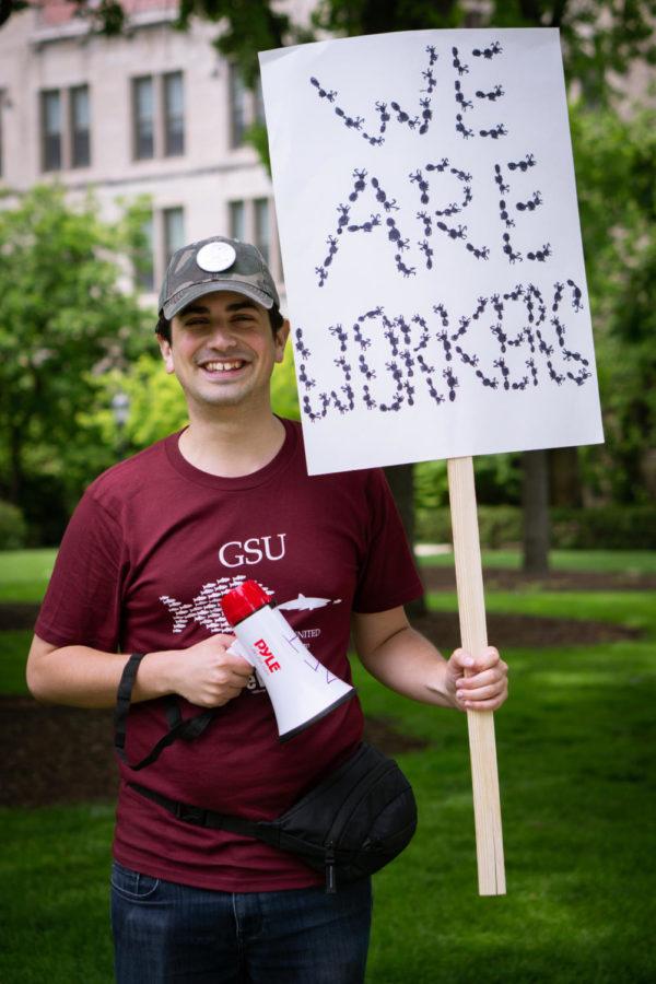 PhD candidate in evolutionary biology Ben Blanchard holds a sign reading We Are Workers, spelled in ants.