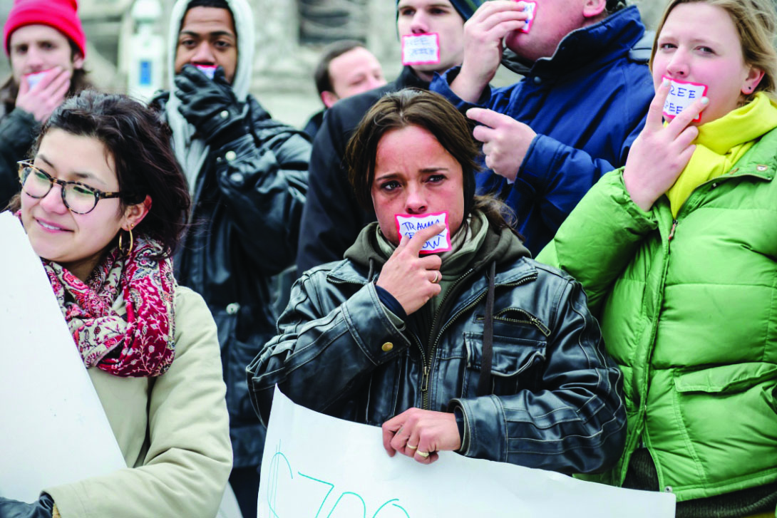 UCPD officer Janelle Marcellis holds a protest sign and wears protest tape over her mouth at a trauma center protest in 2013. She infiltrated the protest to gather intelligence.