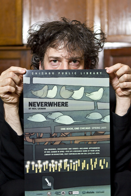 Neil Gaiman holds up a poster for a reading of his book, 