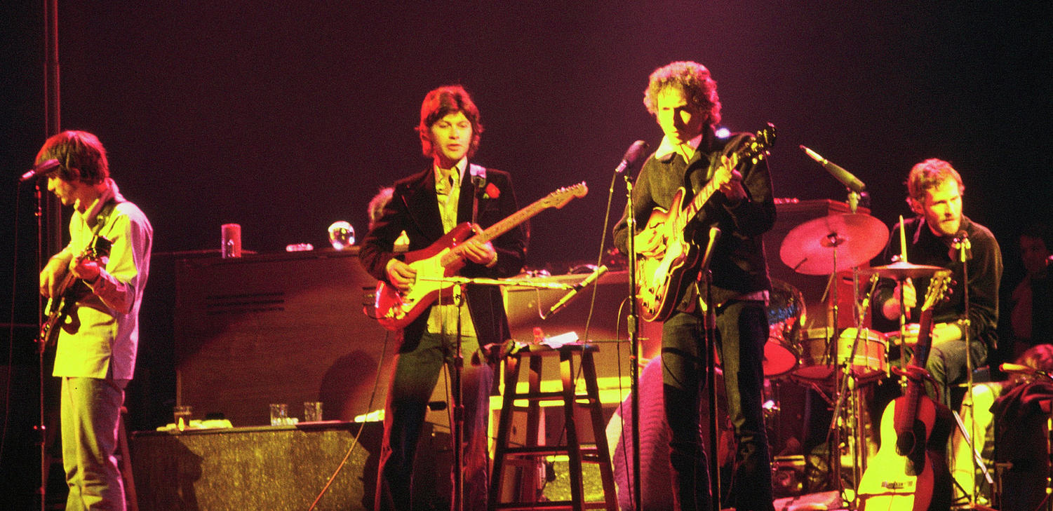 Bob Dylan alongside The Band during a 1974 Chicago performance. From left to right: Rick Danko (bass), Robbie Robertson (guitar), Dylan (guitar), Levon Helm (drums).