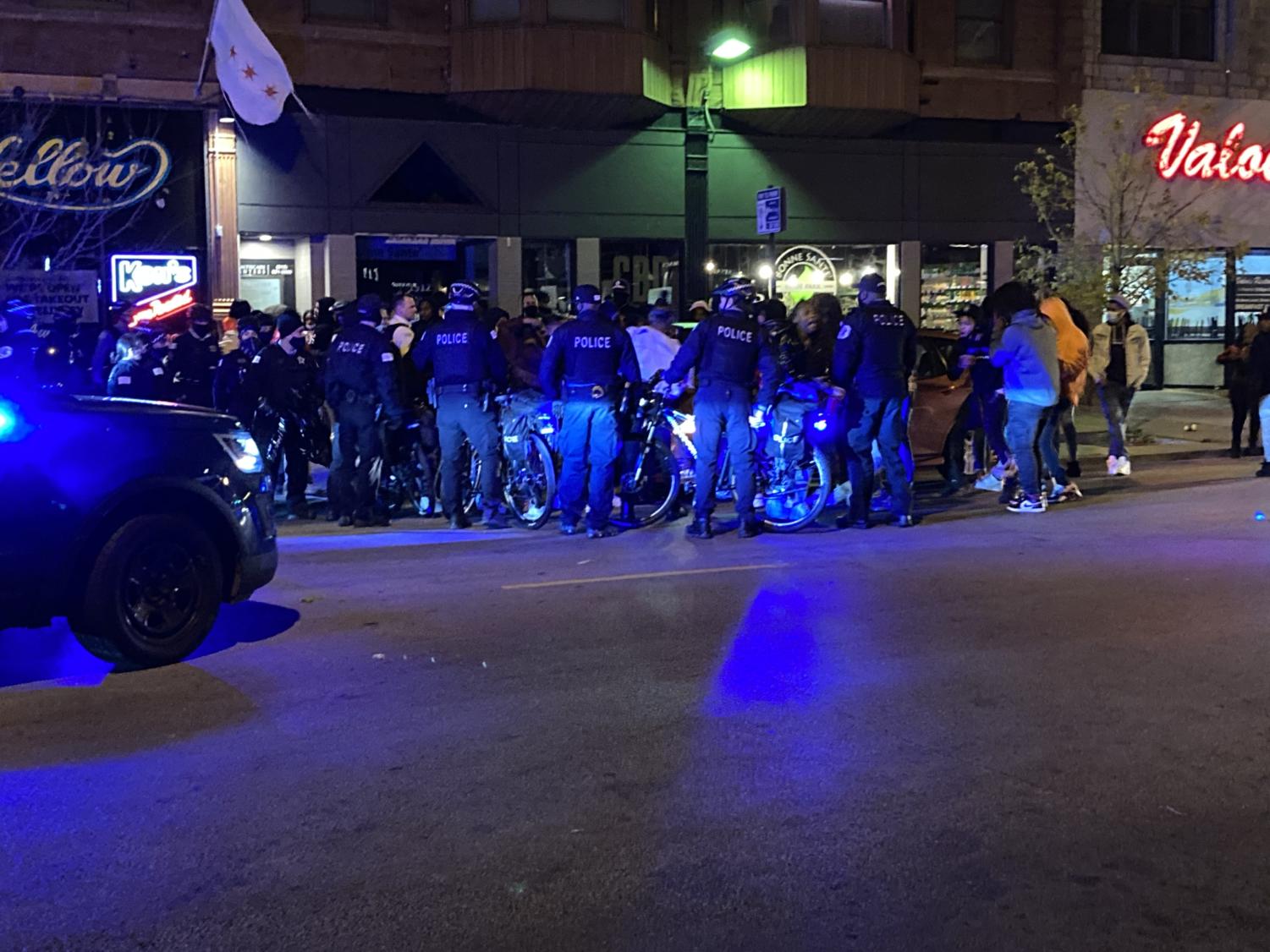 Police surround a battery victim. Moments earlier, a fight broke out among a group of teens being pushed back by a police line.