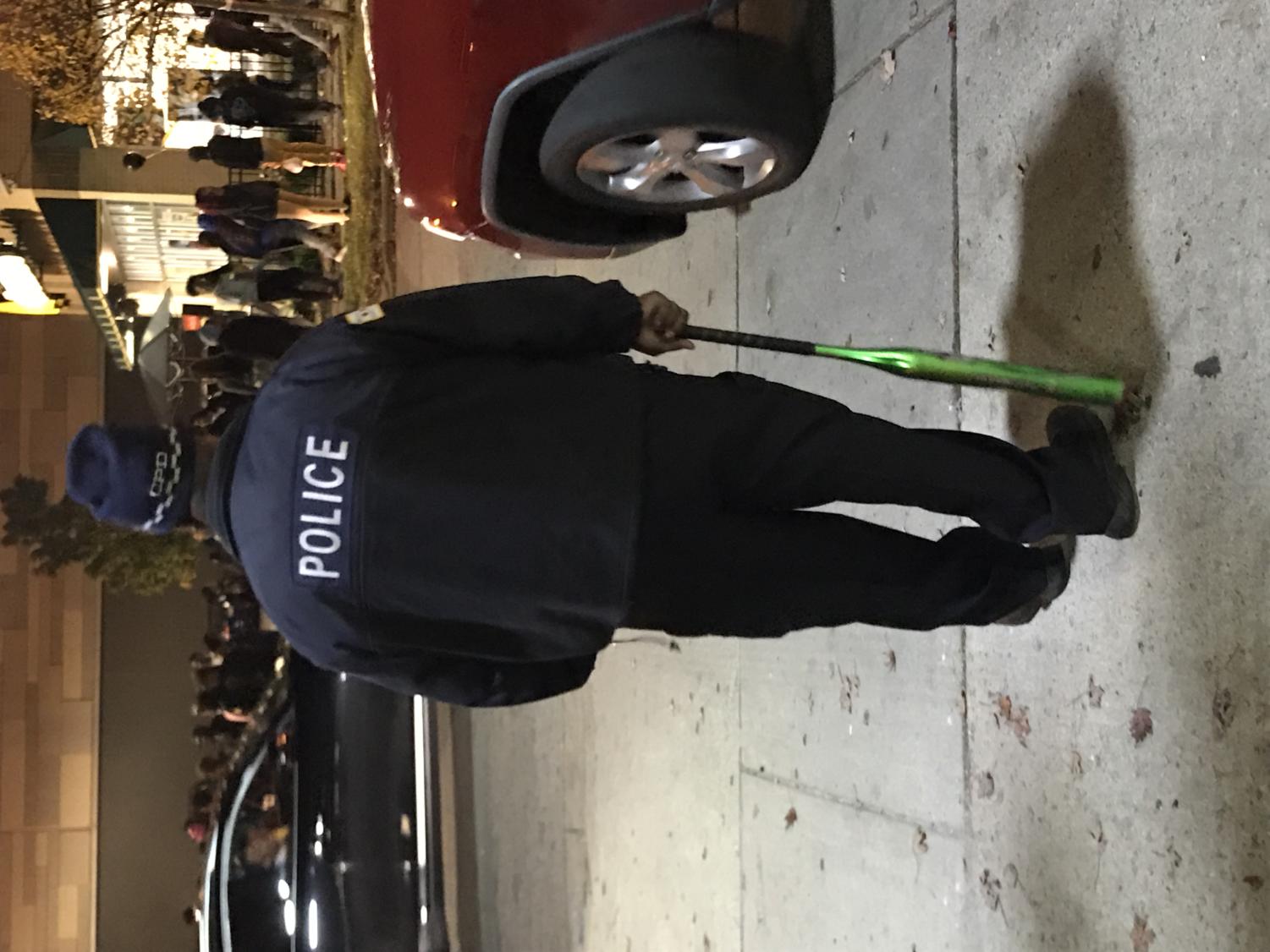 An officer holds a seized metal bat across the street from the McDonald's at 52nd Street and S Lake Park Drive on Monday.