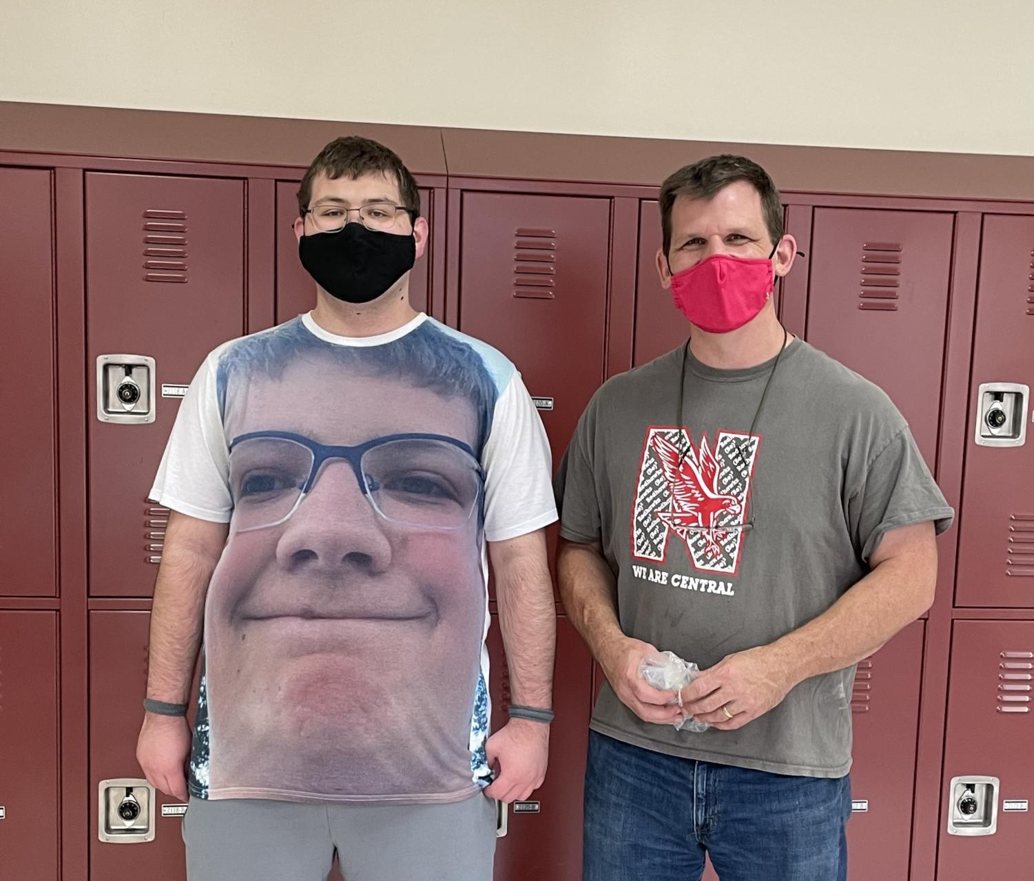 Braden Hajer with his teacher, Seth Brady, in a hallway with crimson lockers behind them. Both are wearing masks.