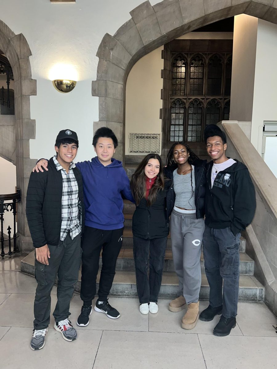 Five students pose for a photo in a half-circle formation in front of a doorway and steps.