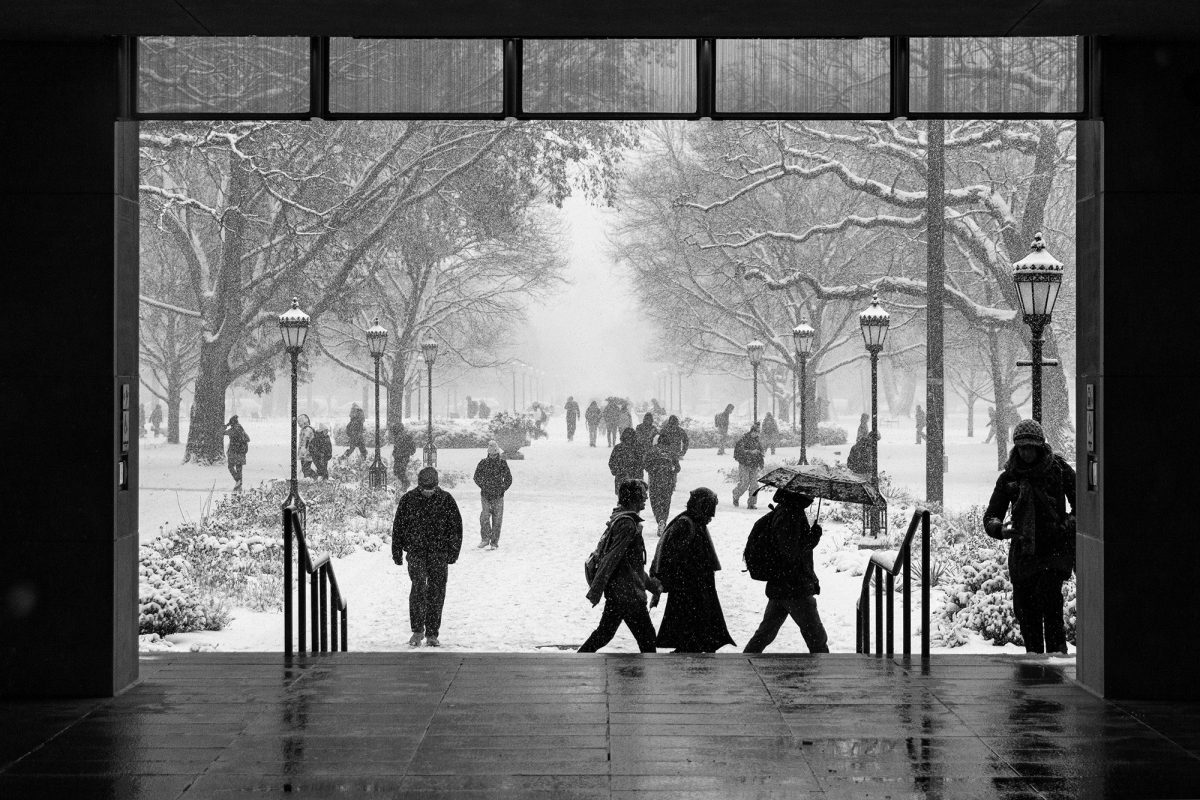 Individuals seen from under the Levi Hall breezeway walk across the snow-covered quad.