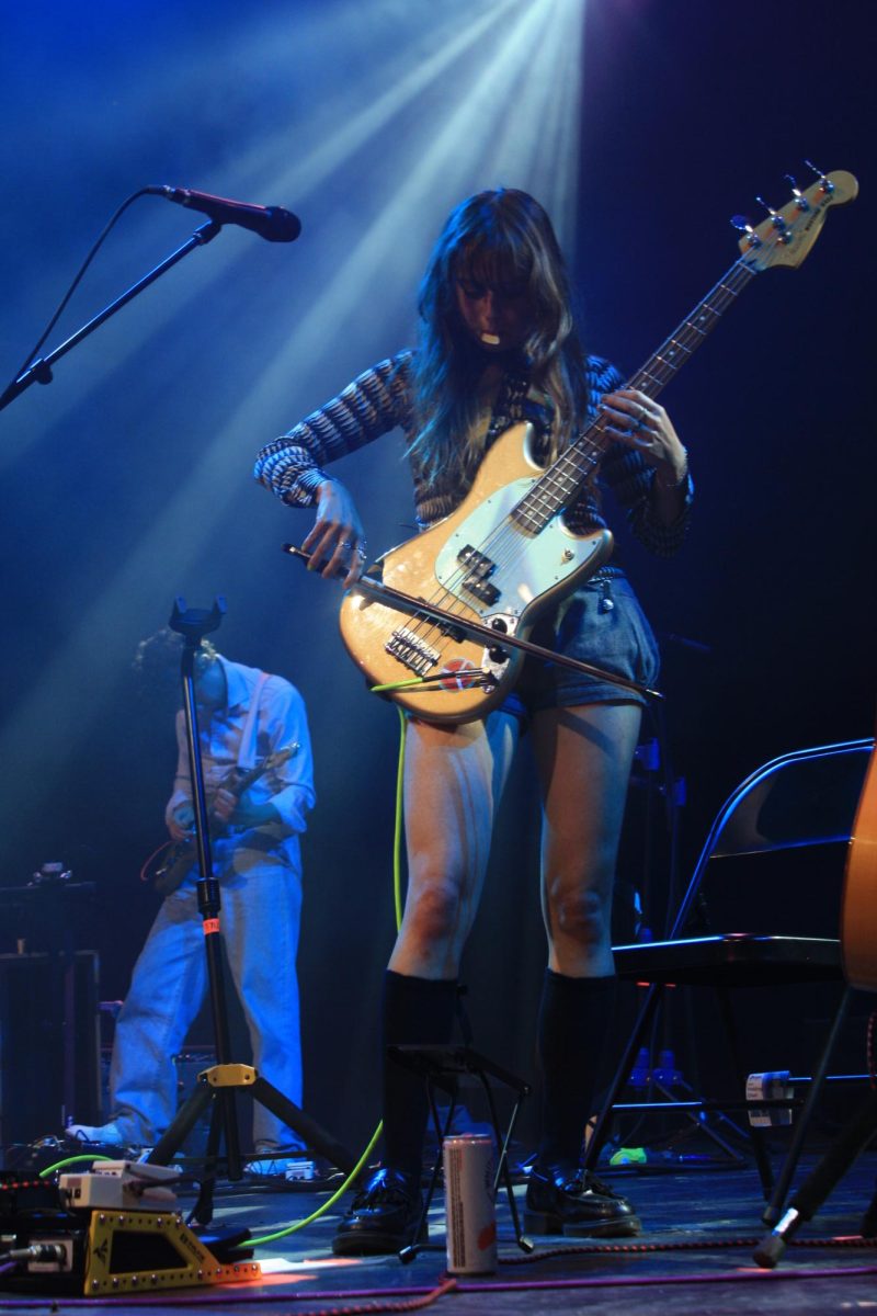 Tyler Hyde, de facto lead vocalist of Black Country, New Road, exemplifies their new sound with her bow poised over the bass strings and her pick hanging out of her mouth. 