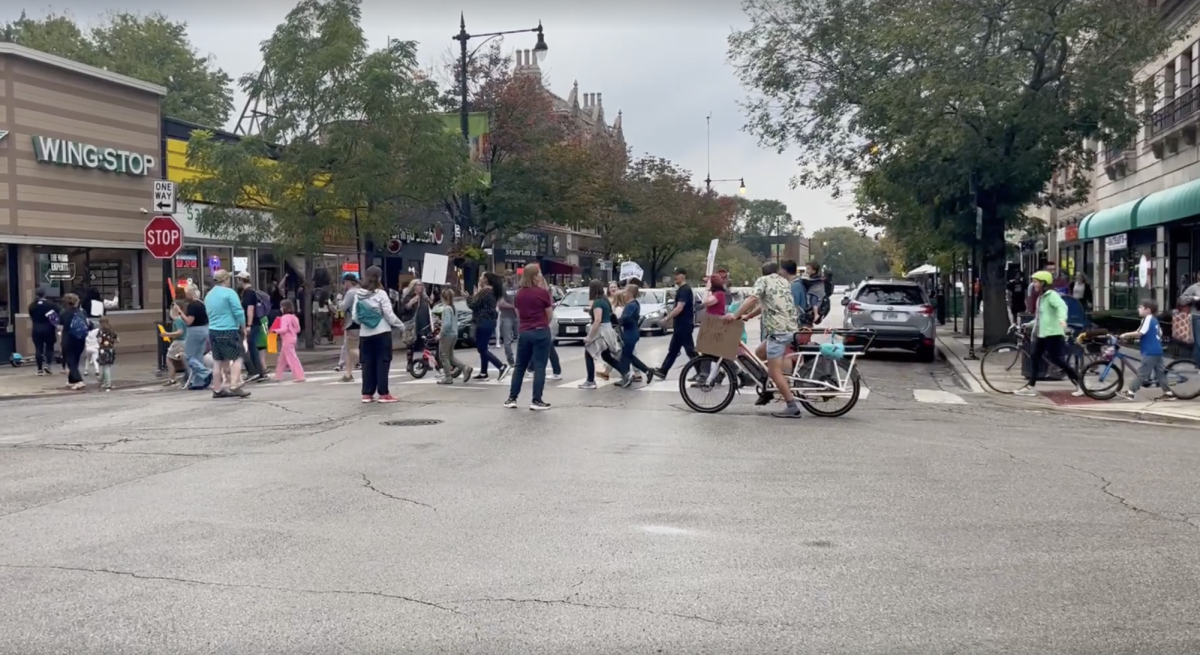 A line of protesters crosses 53rd Street holding signs and bikes.