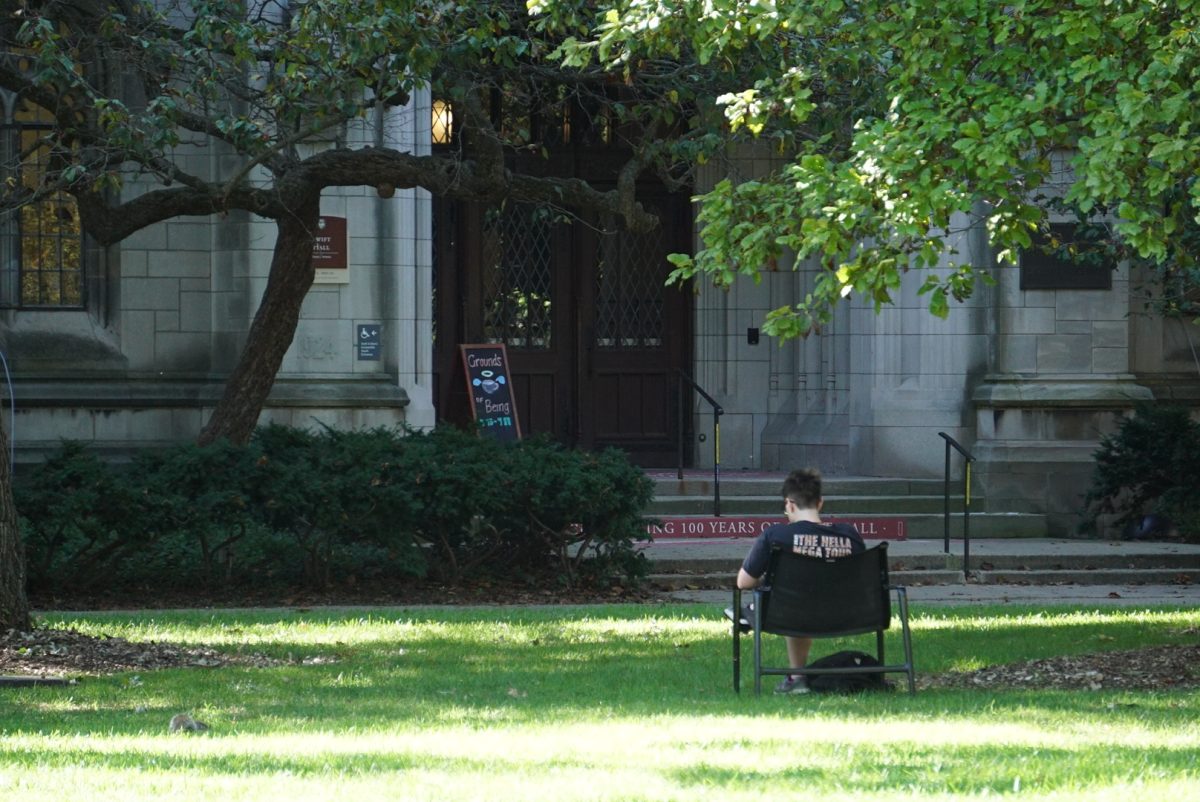 An individual sits on a chair in front of Swift Hall.