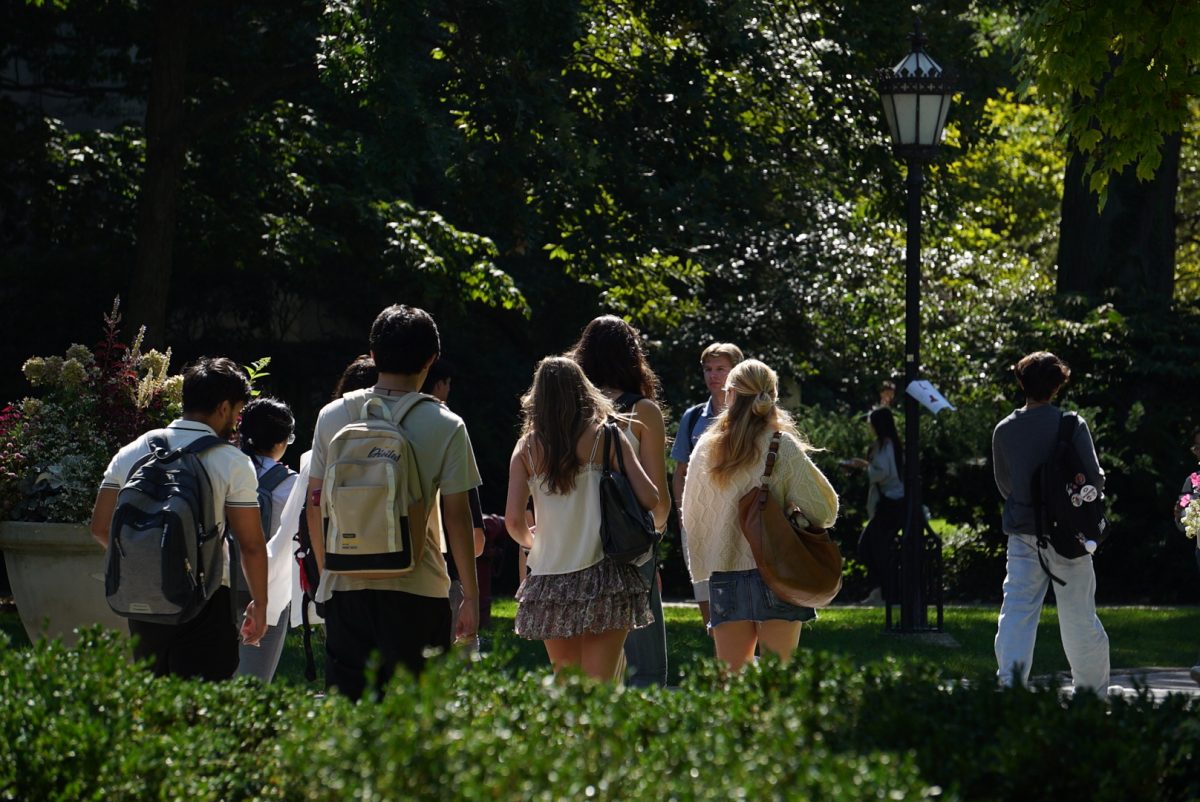 A group of students walks across the main quad towards Harper Memorial Library.
