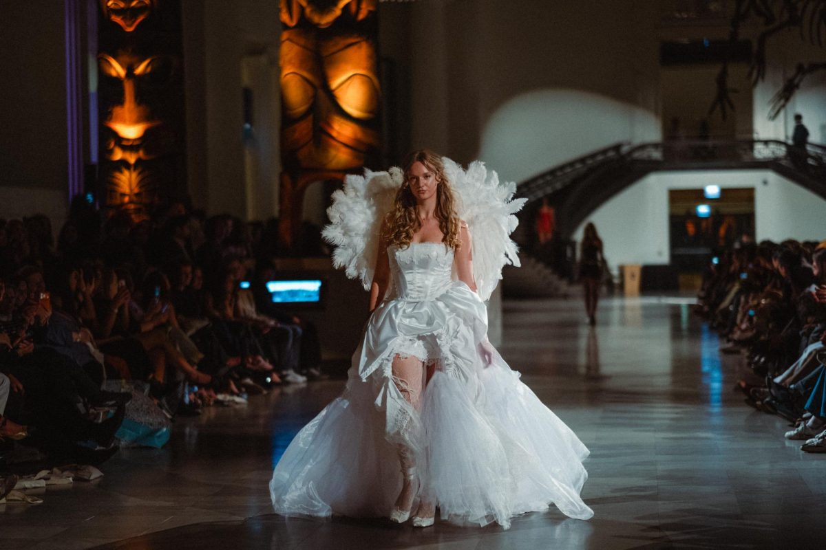 Model (fourth-year Tessa Brummel) dressed in an all-white gown and angel wings walks down the runway. 